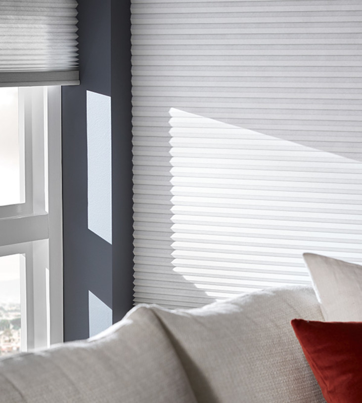 Close up of white honeycomb shades in a bright living room.