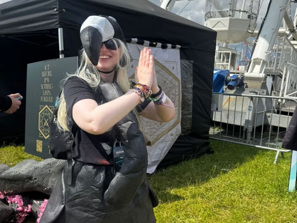 Scarlett, dressed in a vibrant flamingo costume, poses next to a large, illuminated Ferris wheel at a festive event.