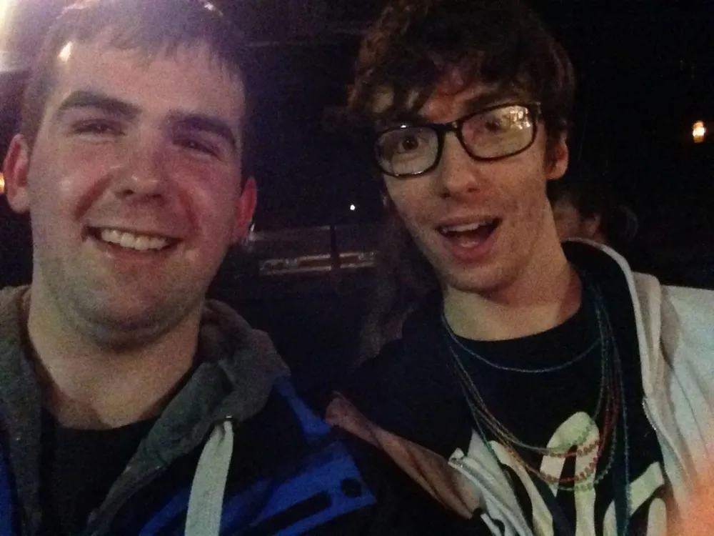 Two young men are smiling at the camera, capturing a joyful and friendly moment between them.