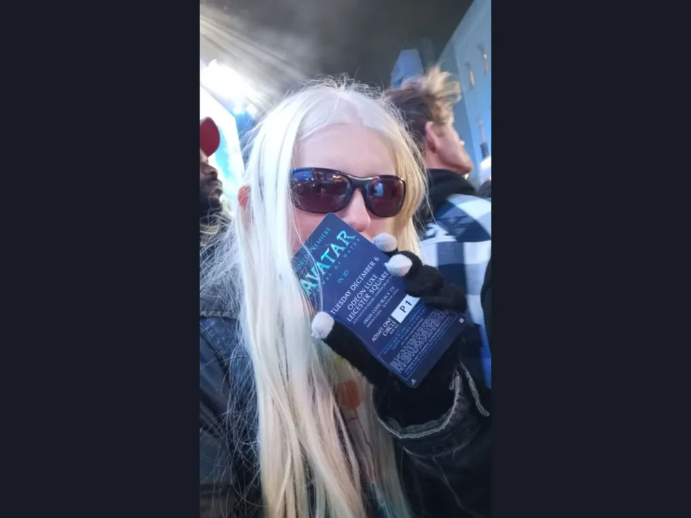 Scarlett standing in a crowd holding up a movie pass for Avatar The Way Of Water in 3D.