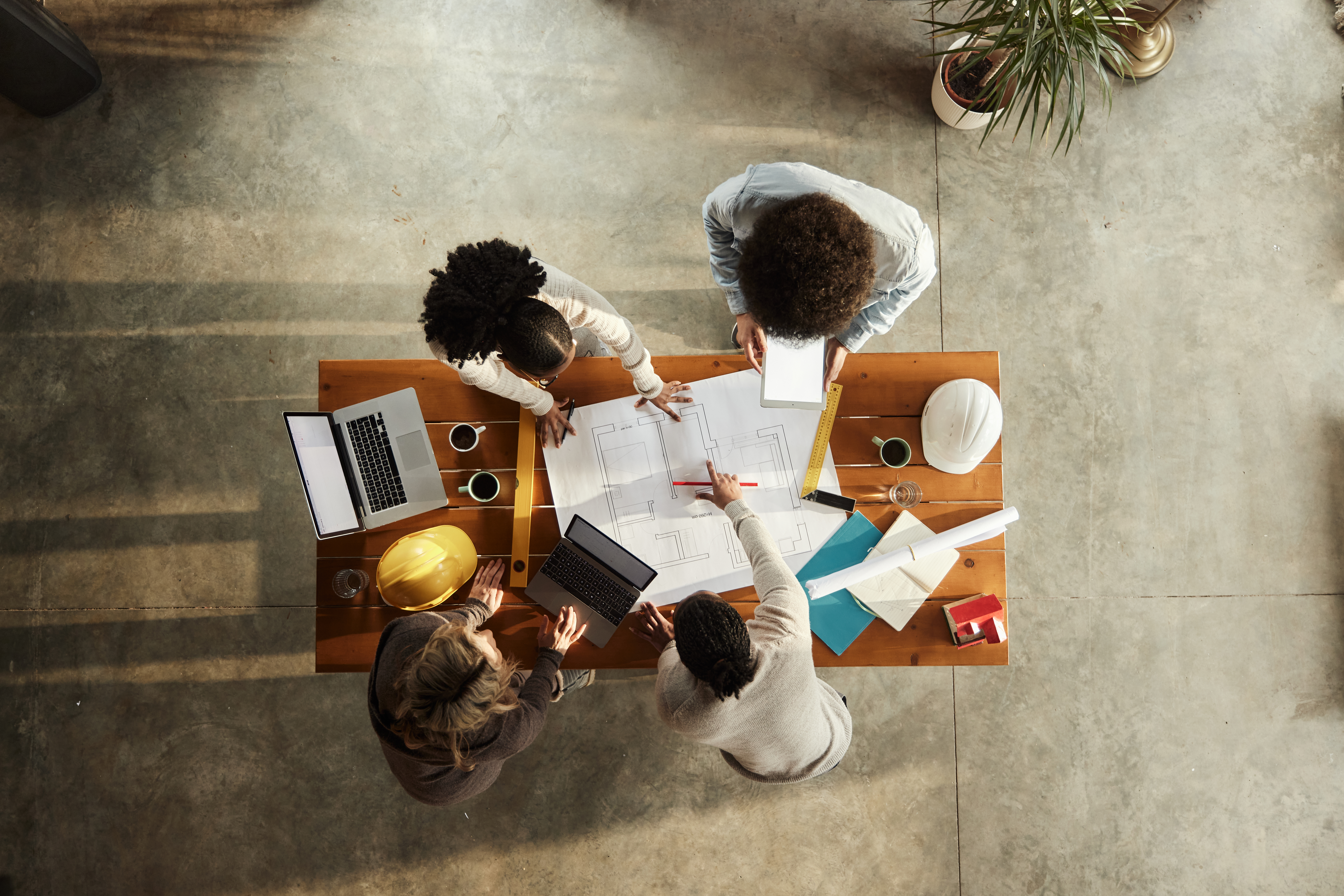 Overhead view of an AEC project team reviewing plans at a table with hard hats and a laptop