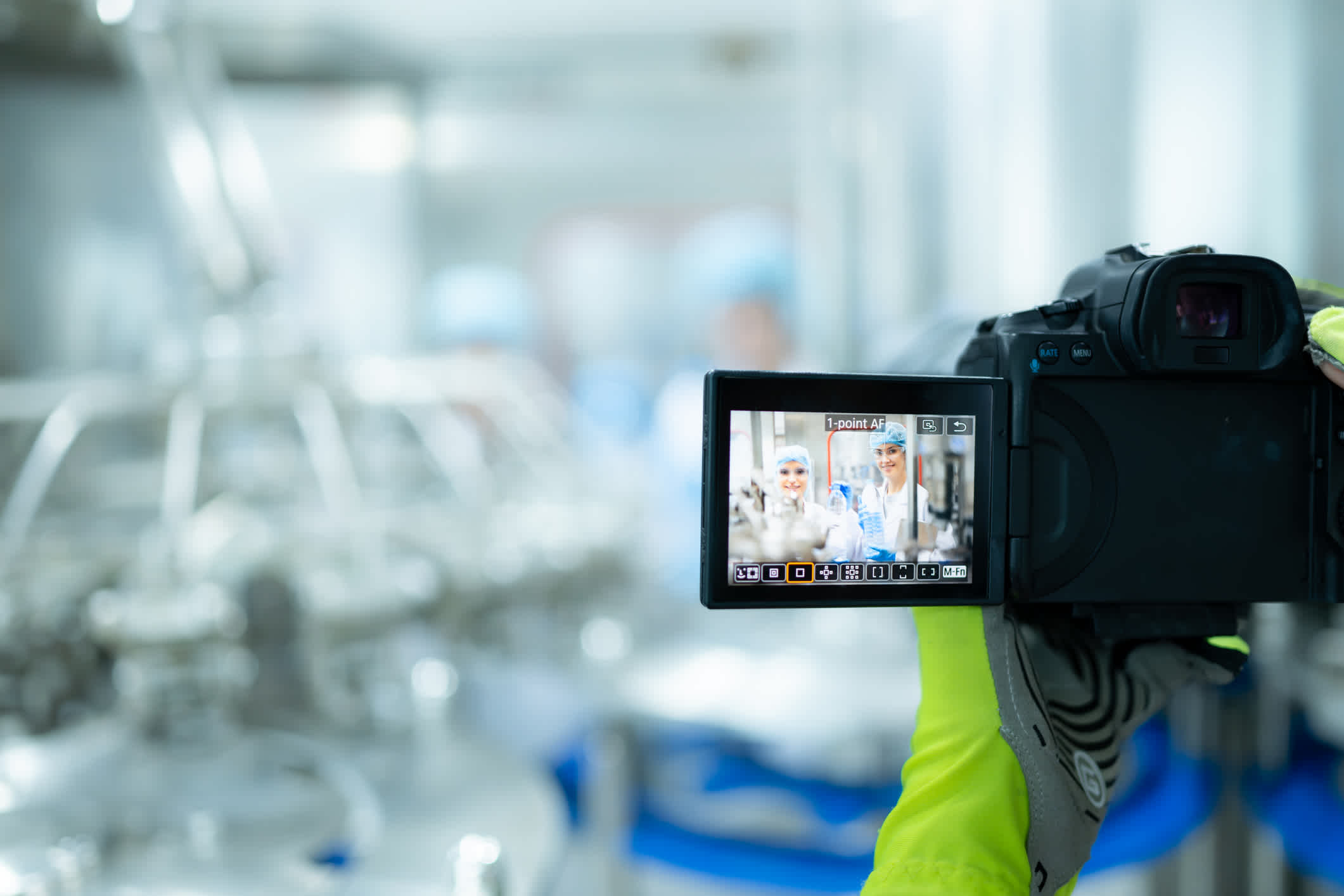 Video marketing of a production line, blurry in the background focused on hands holding a video camera. | Watermark