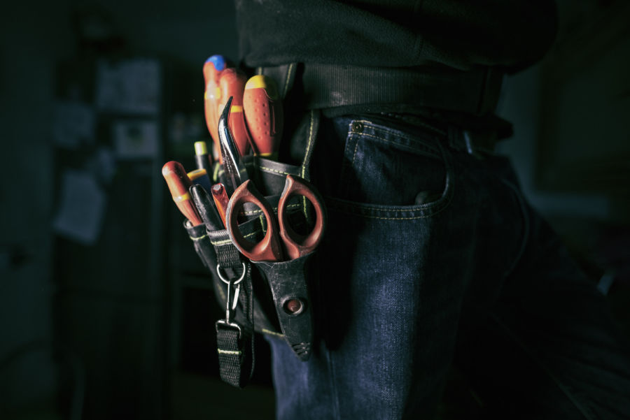 Detail of tools belt of electrician worker at home kitchen in low key screw