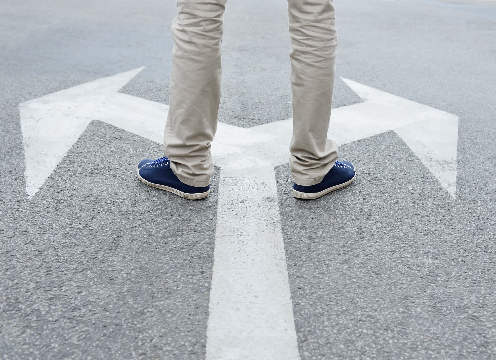 A man standing on arrows painted on asphalt trying to make a decision. | Watermark