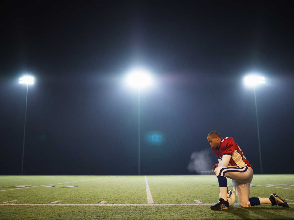 american football player kneeling on field