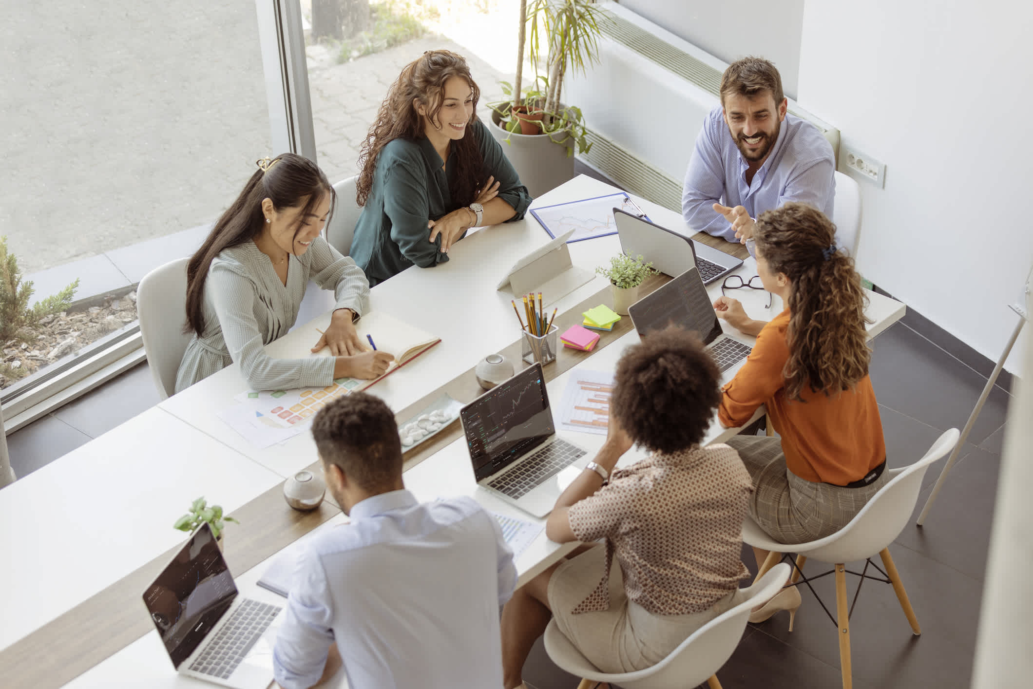 Choosing the right creative digital marketing agency. Showing a photo of diverse business people discussing together while having a meeting around a table in a modern office | Watermark.
