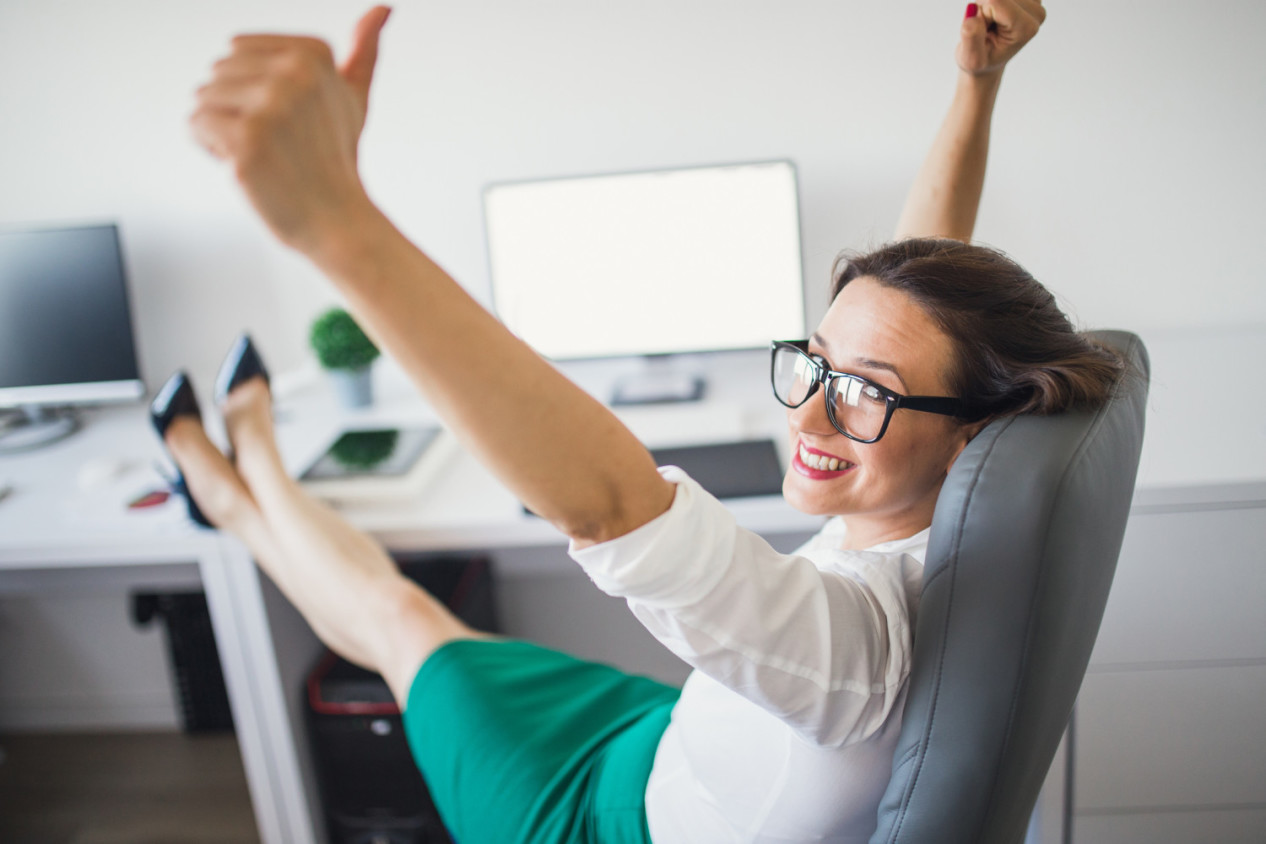 Excited woman raising her arms while working on computer in her office
