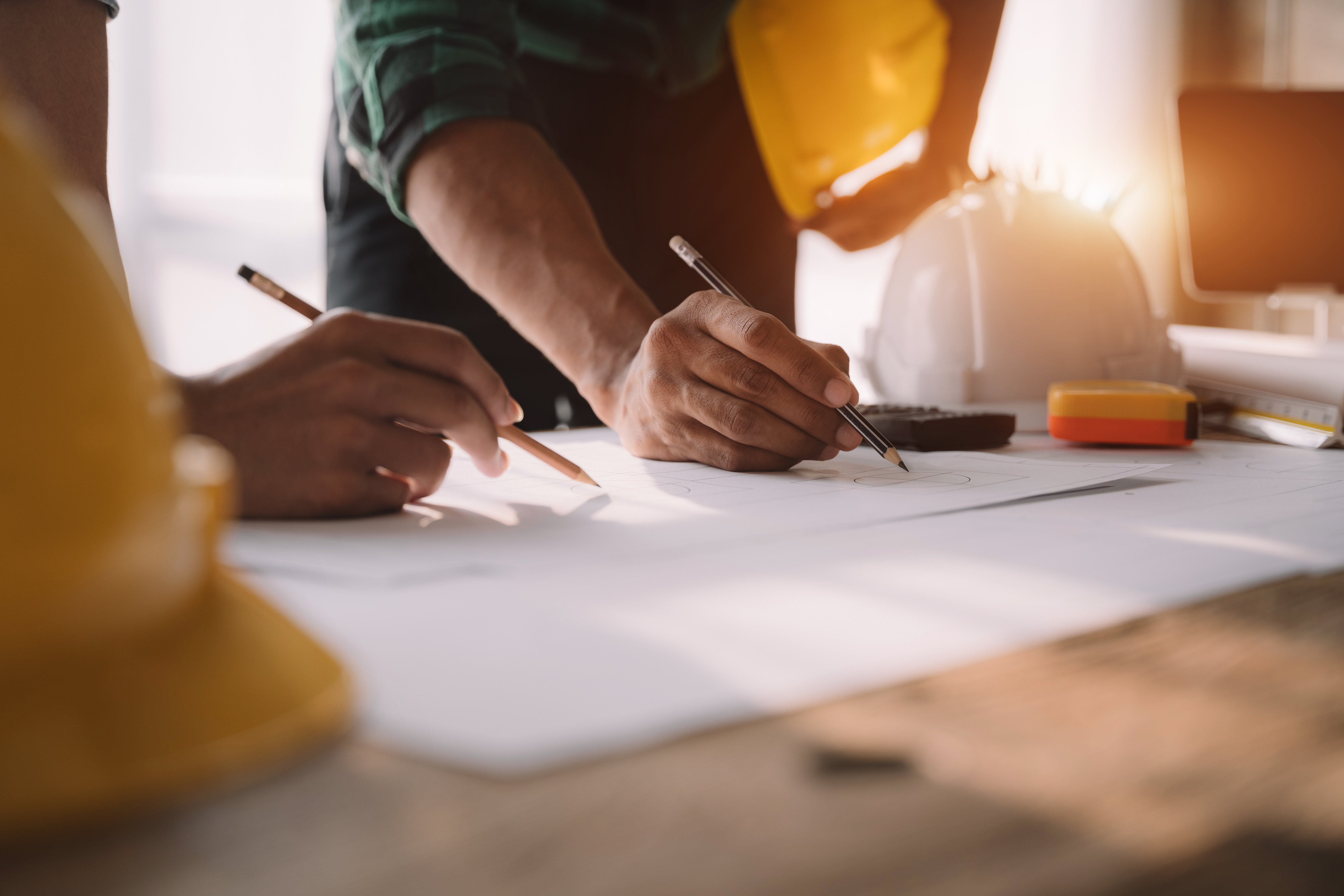 Close-up of architecture and construction professionals collaborating on blueprints at a job site. Safety helmets and tools in the background highlight the real-world setting of AEC businesses. Ideal for illustrating the importance of omnichannel marketing in industries where long sales cycles require consistent branding, trust-building, and cross-platform visibility.