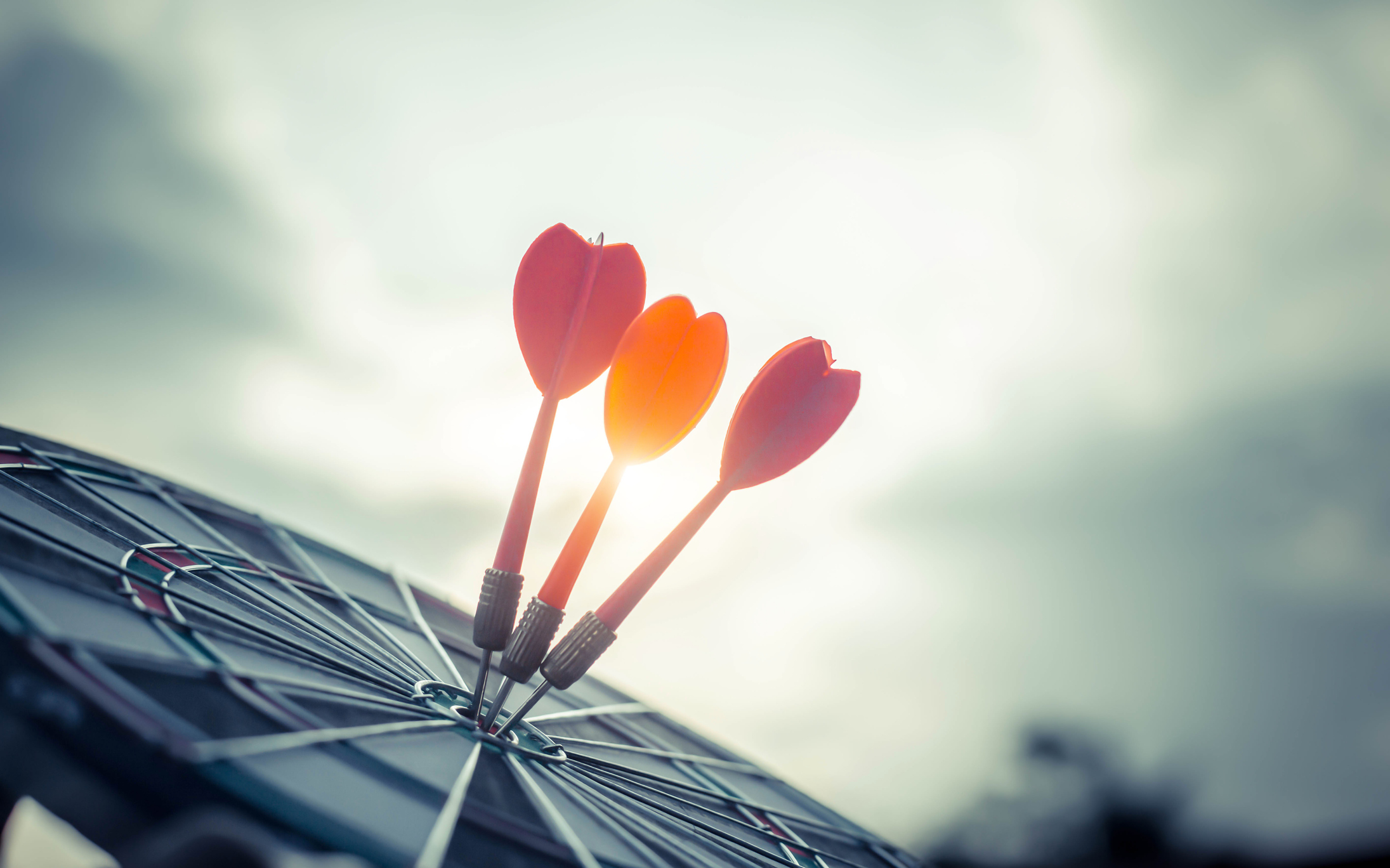 Close up shot of the dart arrow hit on bulleyes of dartboard to represent that the business reached the target with dark tone picture style. Target and goal as concept. | Watermark