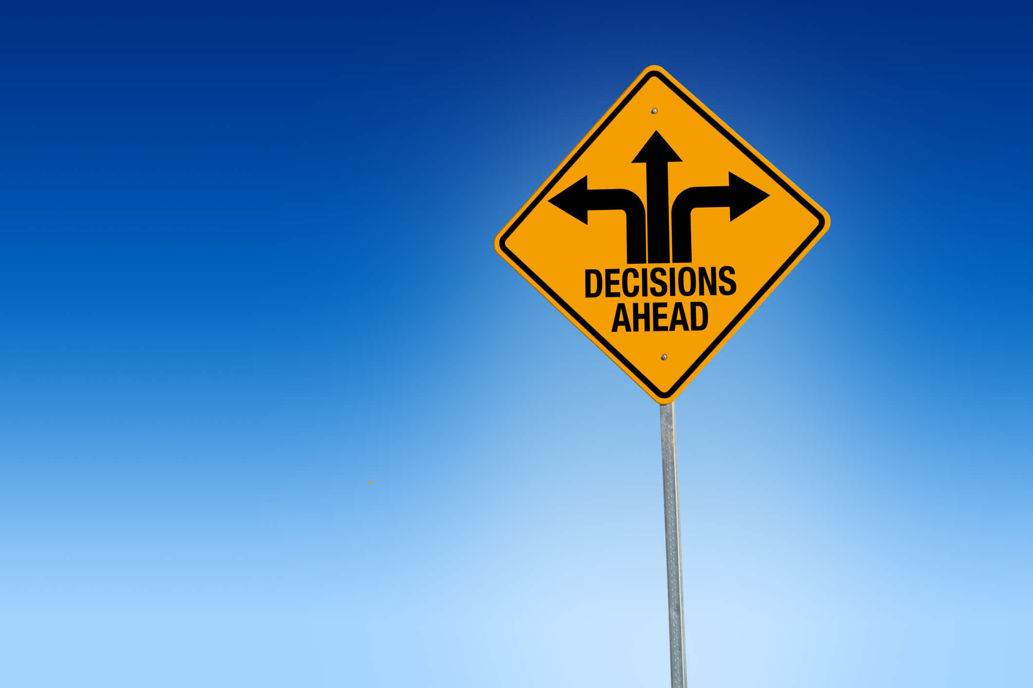 A yellow sign with arrows pointing straight, left, and right, and the words ‘decisions ahead’ with a blue background. | Watermark