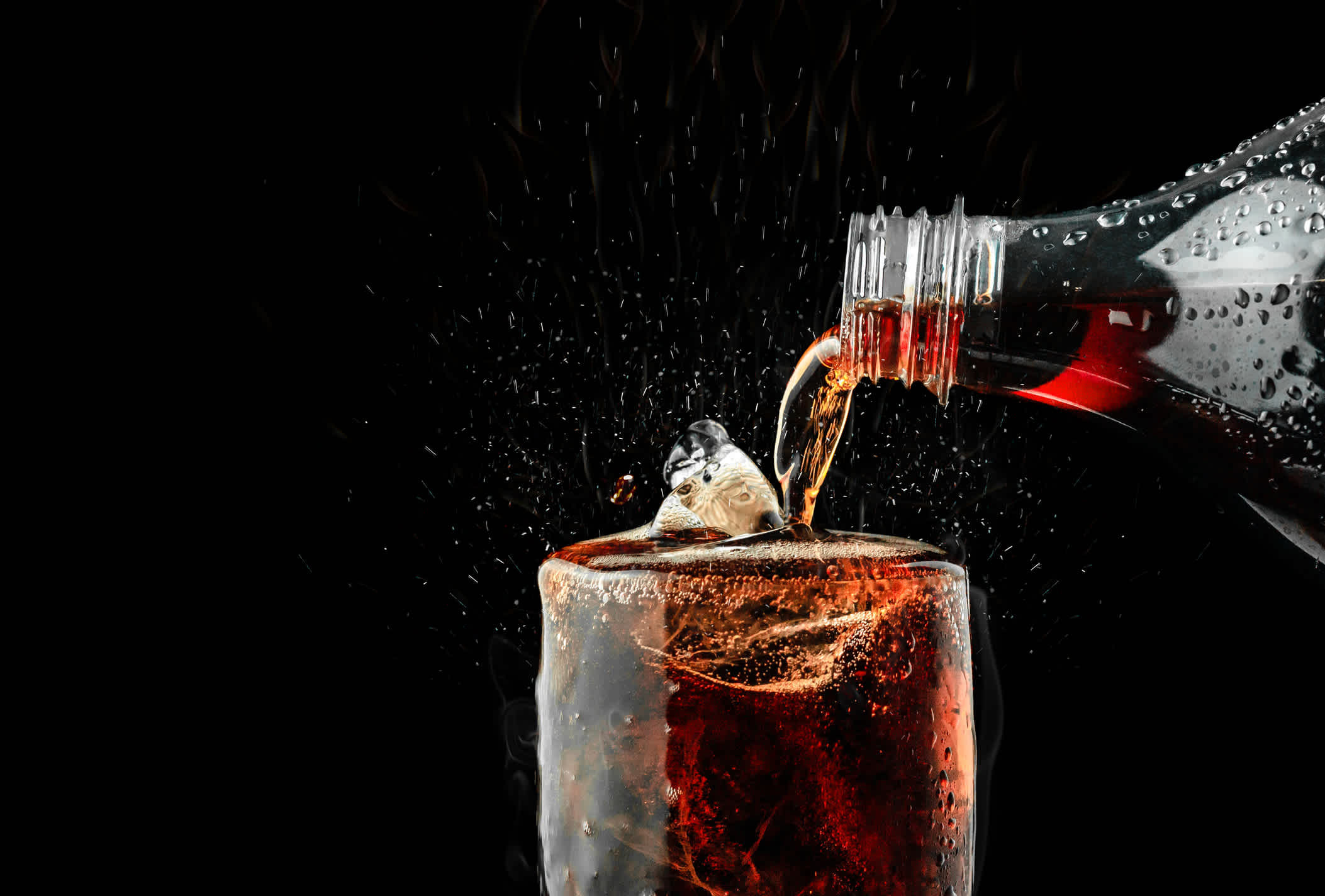 Pour soft drink in glass with ice splash on dark background. | Watermark