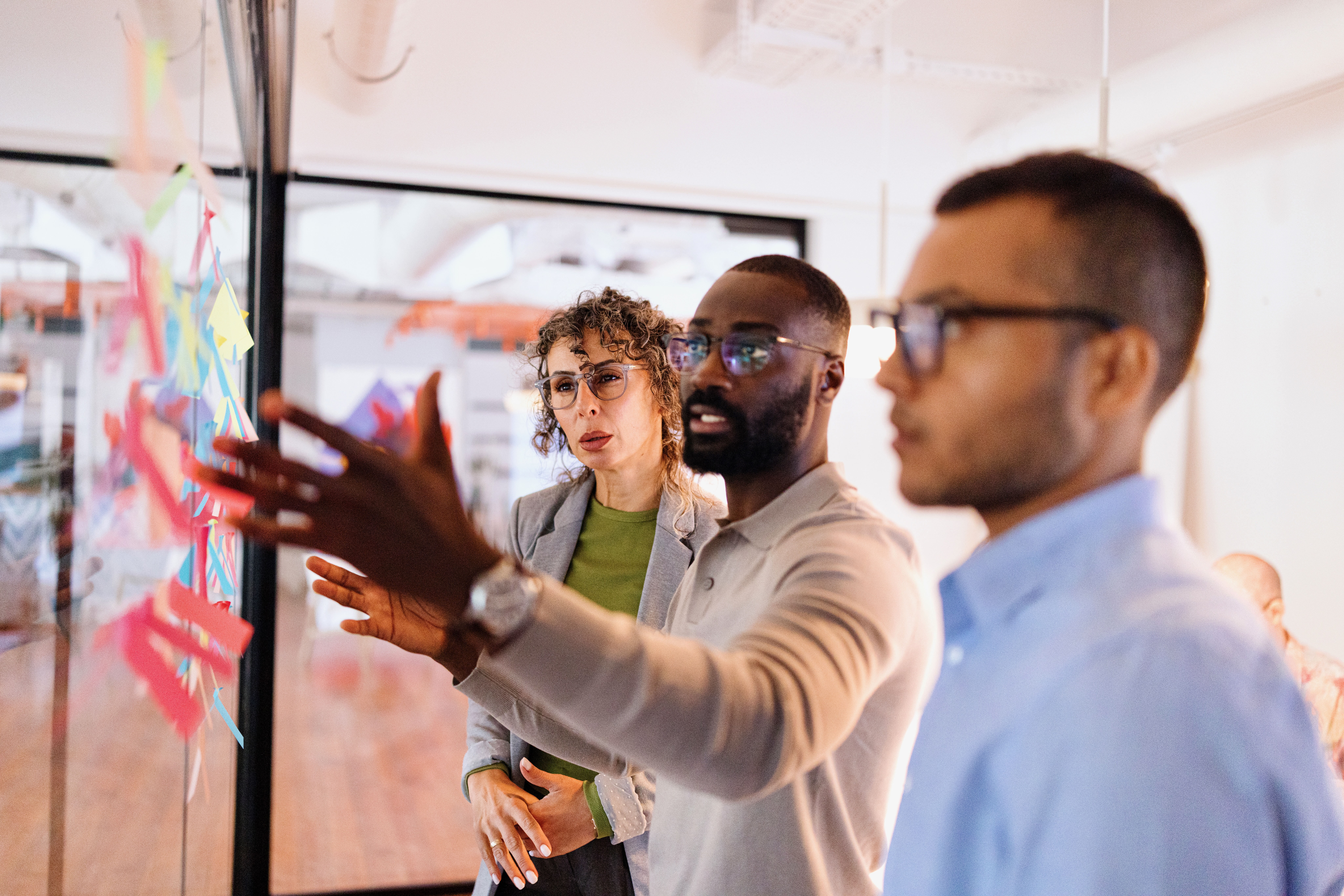 Marketing team reviewing colorful sticky notes on a glass wall while planning a customer journey