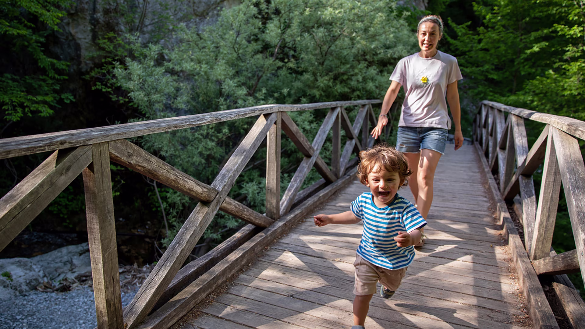 Kind läuft lachend über eine Holzbrücke im Wald – Bewegung im Alltag spielerisch mit der Familie erleben.