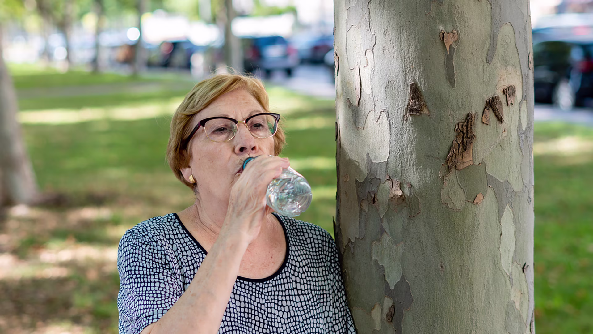 Ältere Frau trinkt im Freien Wasser aus einer Flasche.