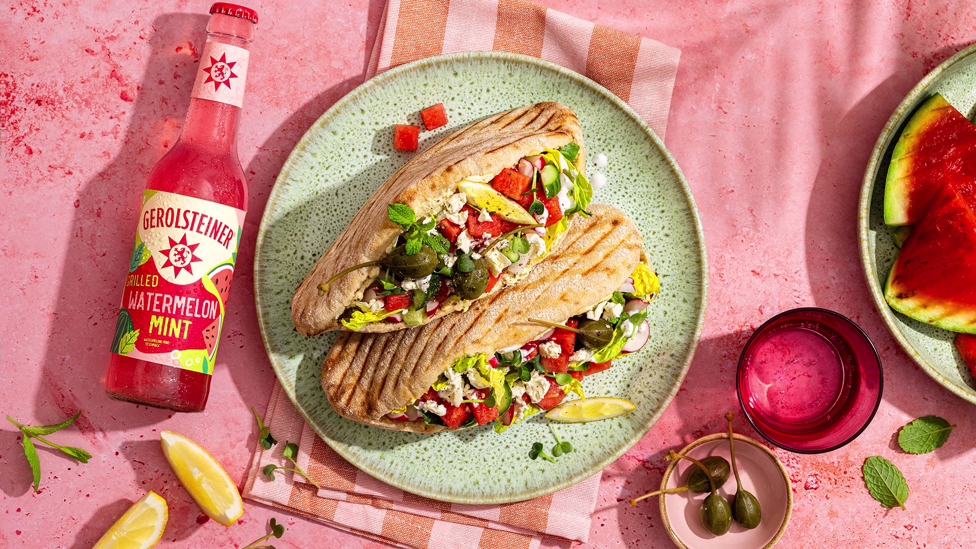 Gefüllte Pitataschen mit frischem Gemüse, Wassermelone und würzigem Käse auf einem sommerlichen Arrangement. Begleitet von einer Gerolsteiner Grilled Watermelon Mint Limonade für ein fruchtig-frisches Geschmackserlebnis.