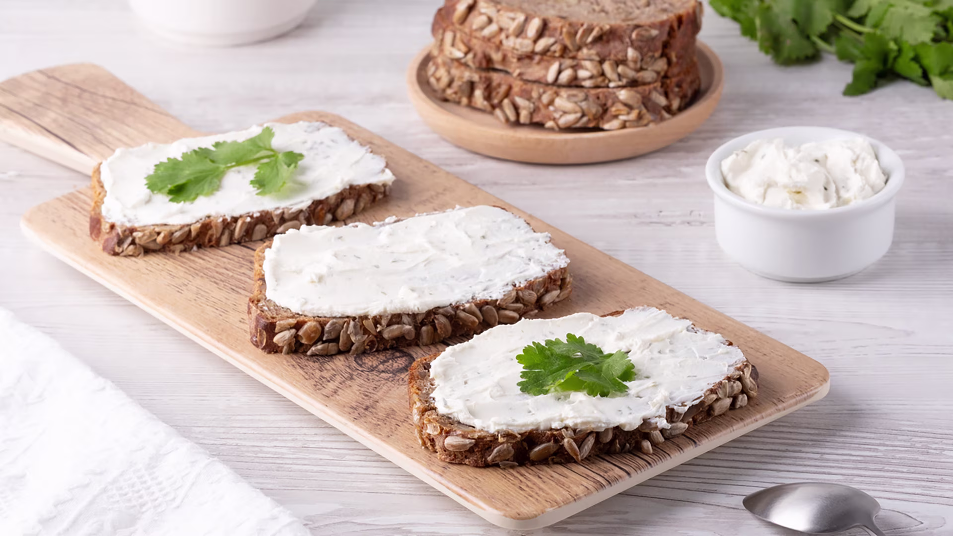 Vollkornbrot-Scheiben mit Frischkäse und Petersilie auf einem Holzbrett