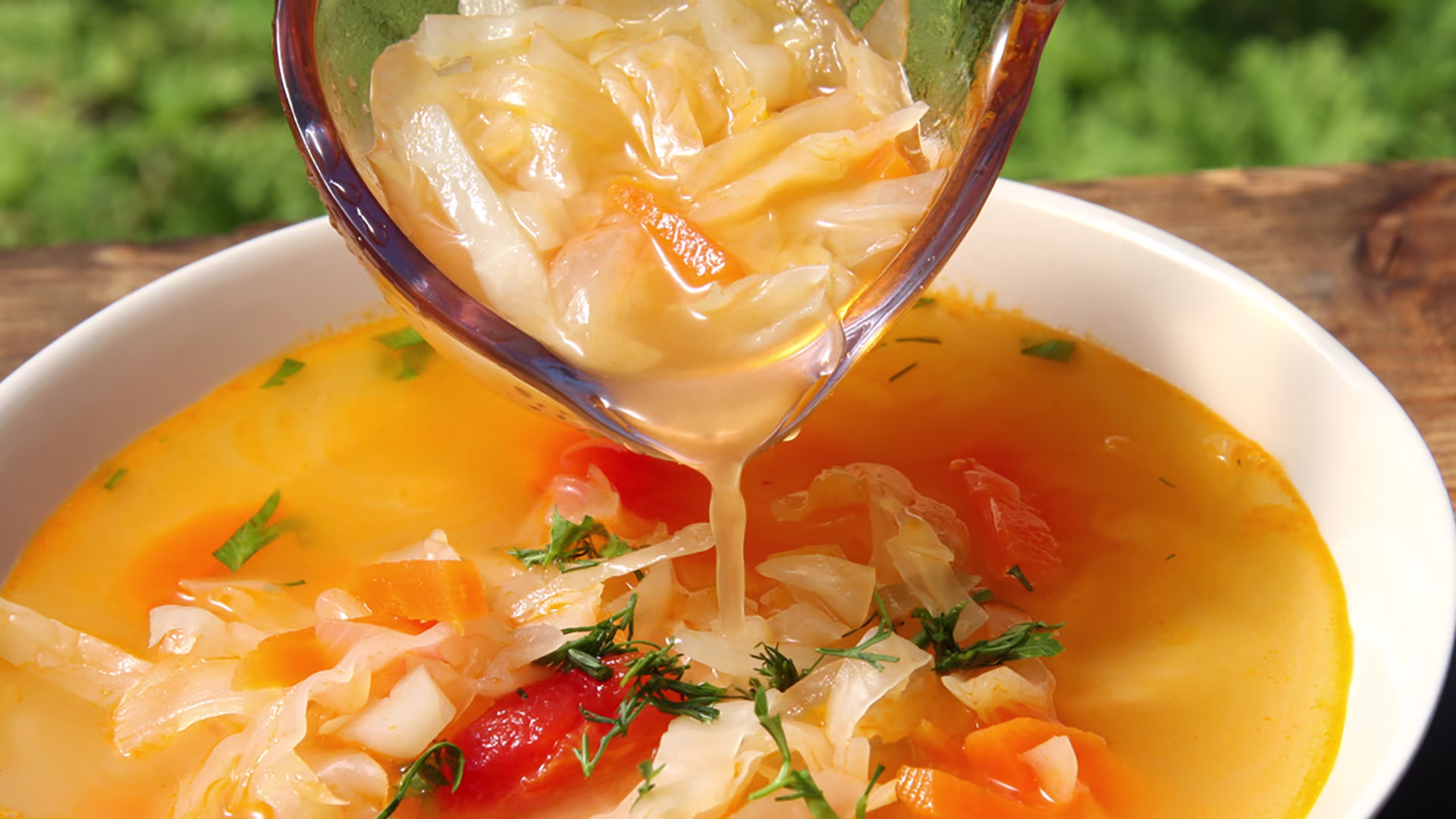 Hände halten einen Teller mit grüner Kohlsuppe