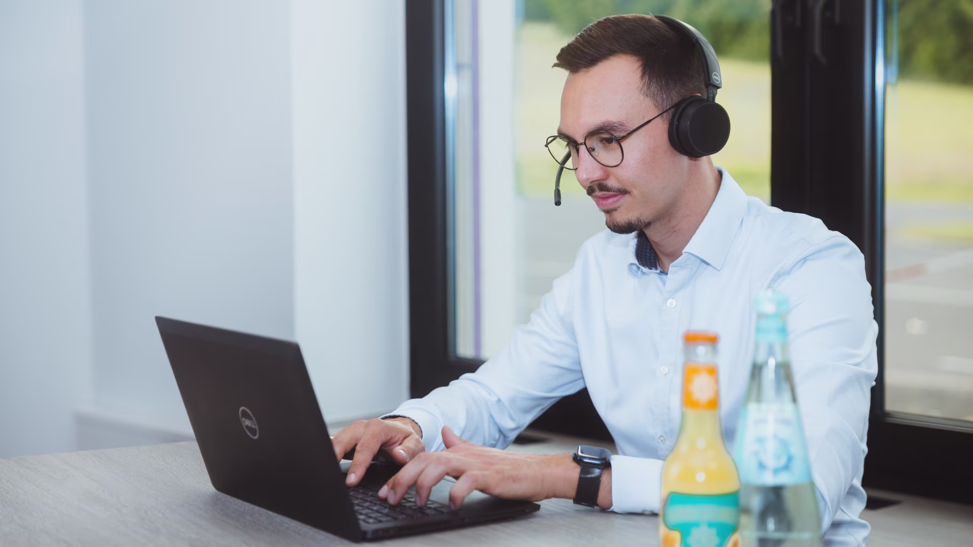Mitarbeitende Person arbeitet mit Headset und Laptop in einer modernen Büroumgebung.