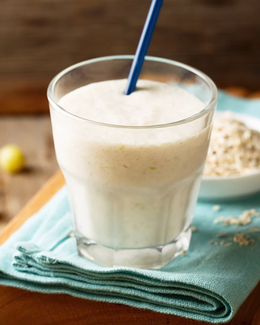 Reisprotein-Vanille-Shake in einem Glas mit Strohhalm auf einem Holztisch.