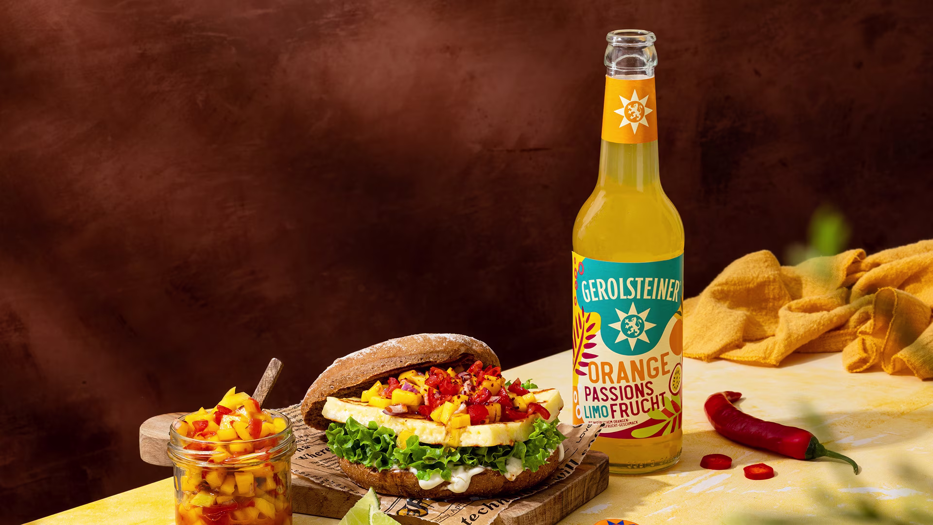 Saftiger Burger mit Grillkäse, frischer Mango-Salsa und knackigem Salat auf rustikalem Brot. Dazu eine fruchtige Gerolsteiner Orange-Passionsfrucht-Limonade für sommerlich-frischen Genuss.
