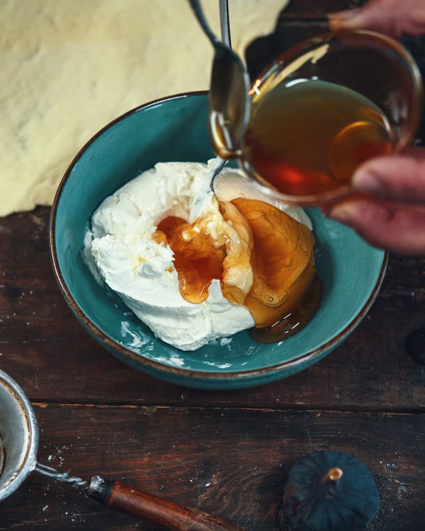 Eine Person gießt Honig als Zuckeralternative in eine Schüssel mit griechischem Joghurt.