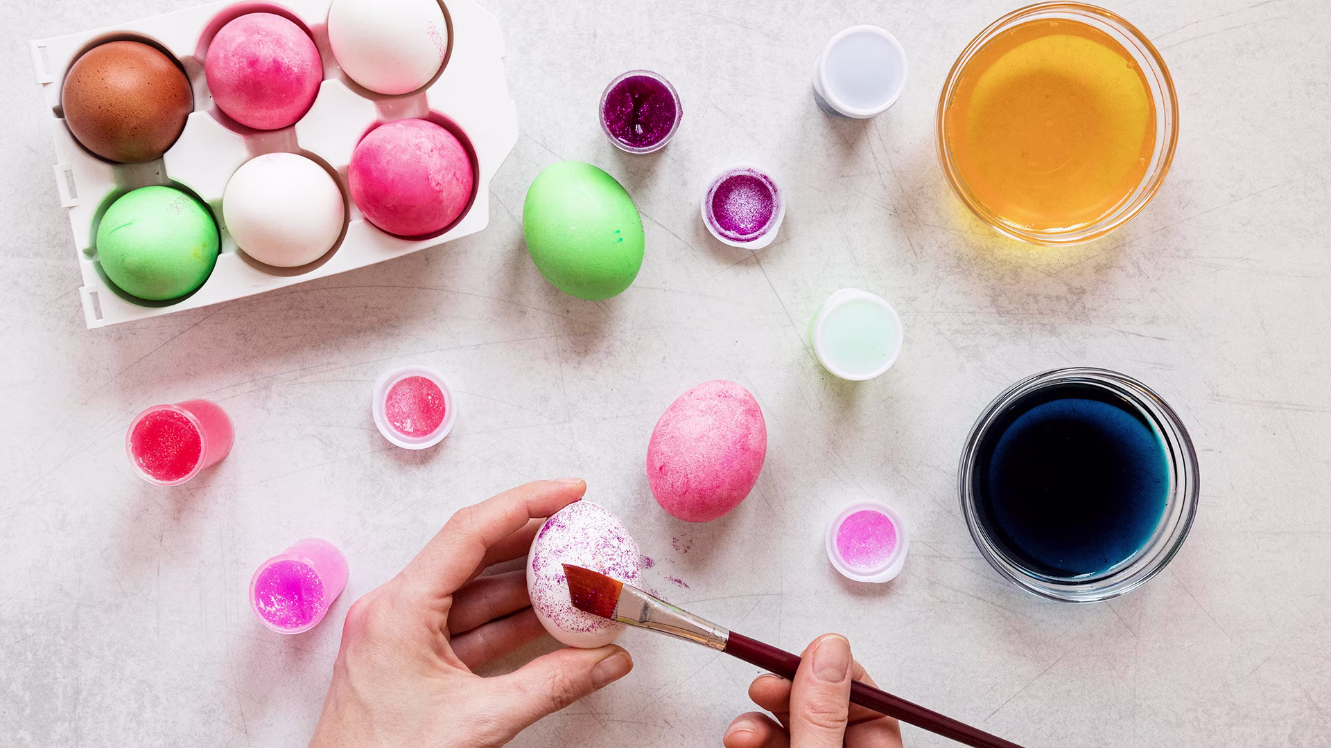 Beim kreativen Gestalten von Ostereiern werden mit Pinsel und Farben individuelle Muster auf die Eier aufgetragen. Bunte Farbtöpfe und bereits gefärbte Eier sorgen für eine fröhliche Osterstimmung.