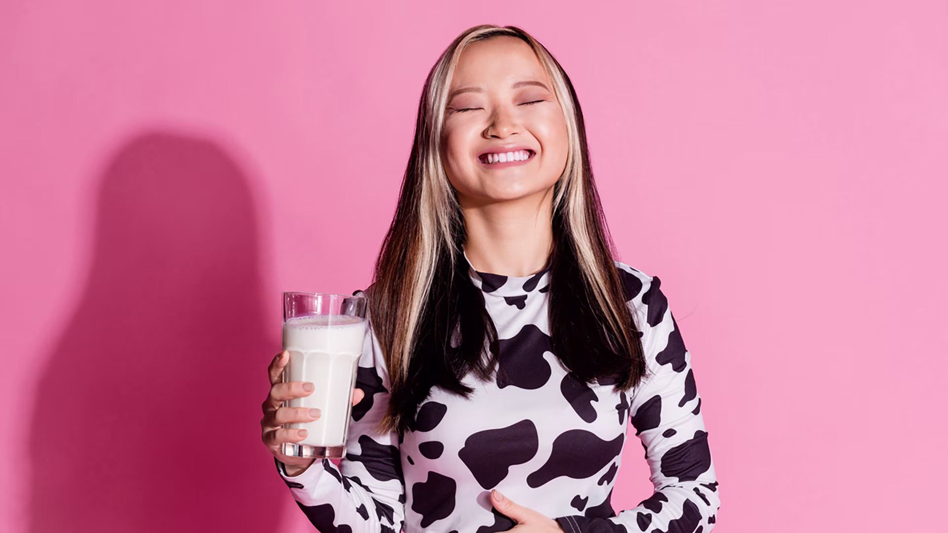 Glückliche Frau hält ein Glas Kefir und hält sich eine Hand auf den Bauch, da Kefir dem Darm guttut.