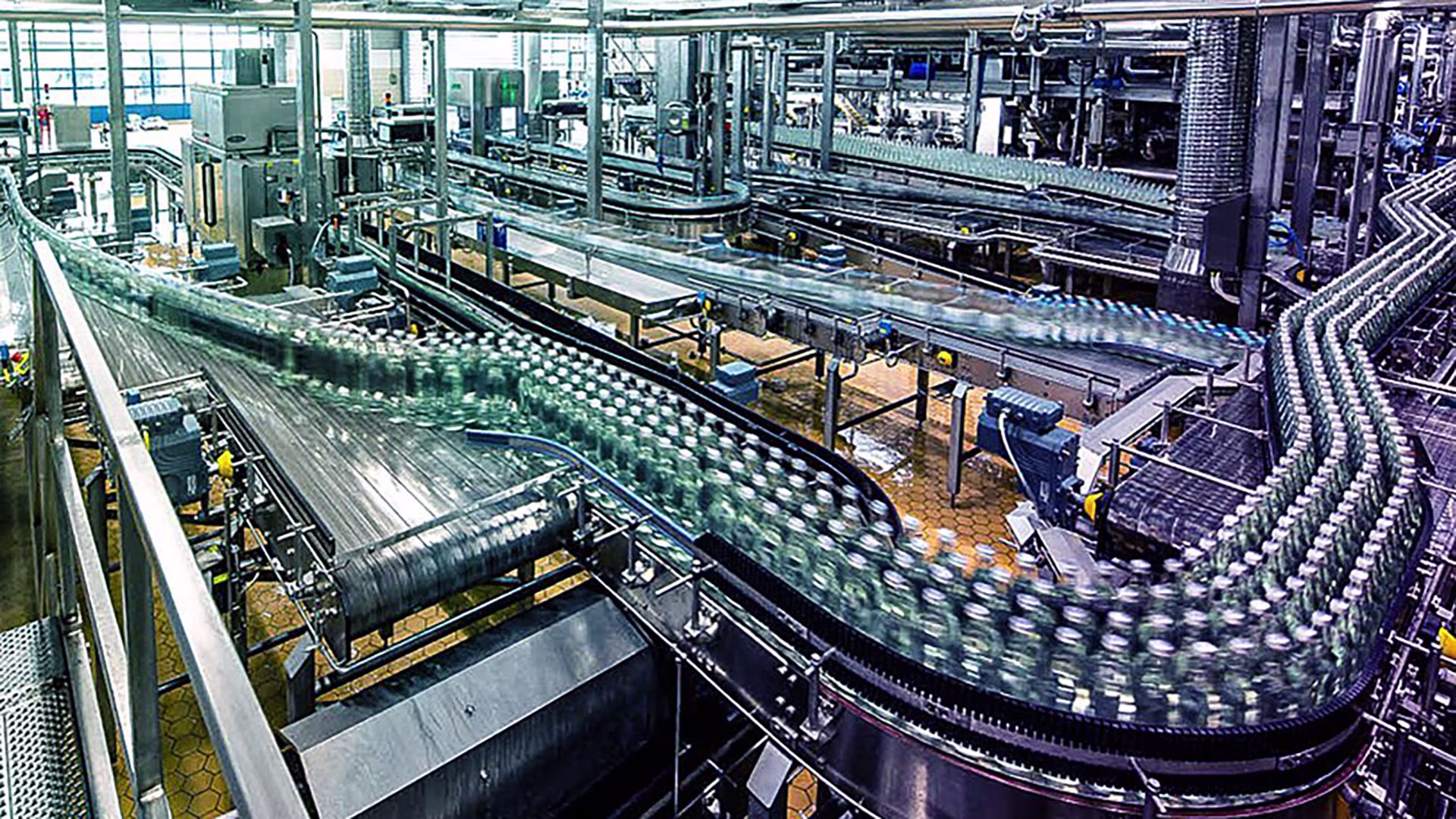 Blick in eine moderne Abfüllanlage mit zahlreichen Glasflaschen auf einem Fließband in Bewegung, umgeben von Edelstahltechnik und Förderanlagen.