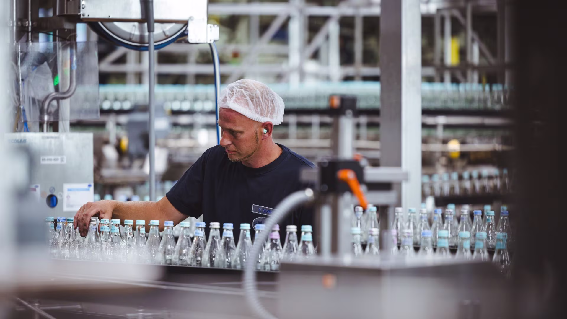 Mitarbeitende Person überwacht und kontrolliert den Produktionsprozess an einer Abfüllanlage für Mineralwasser.