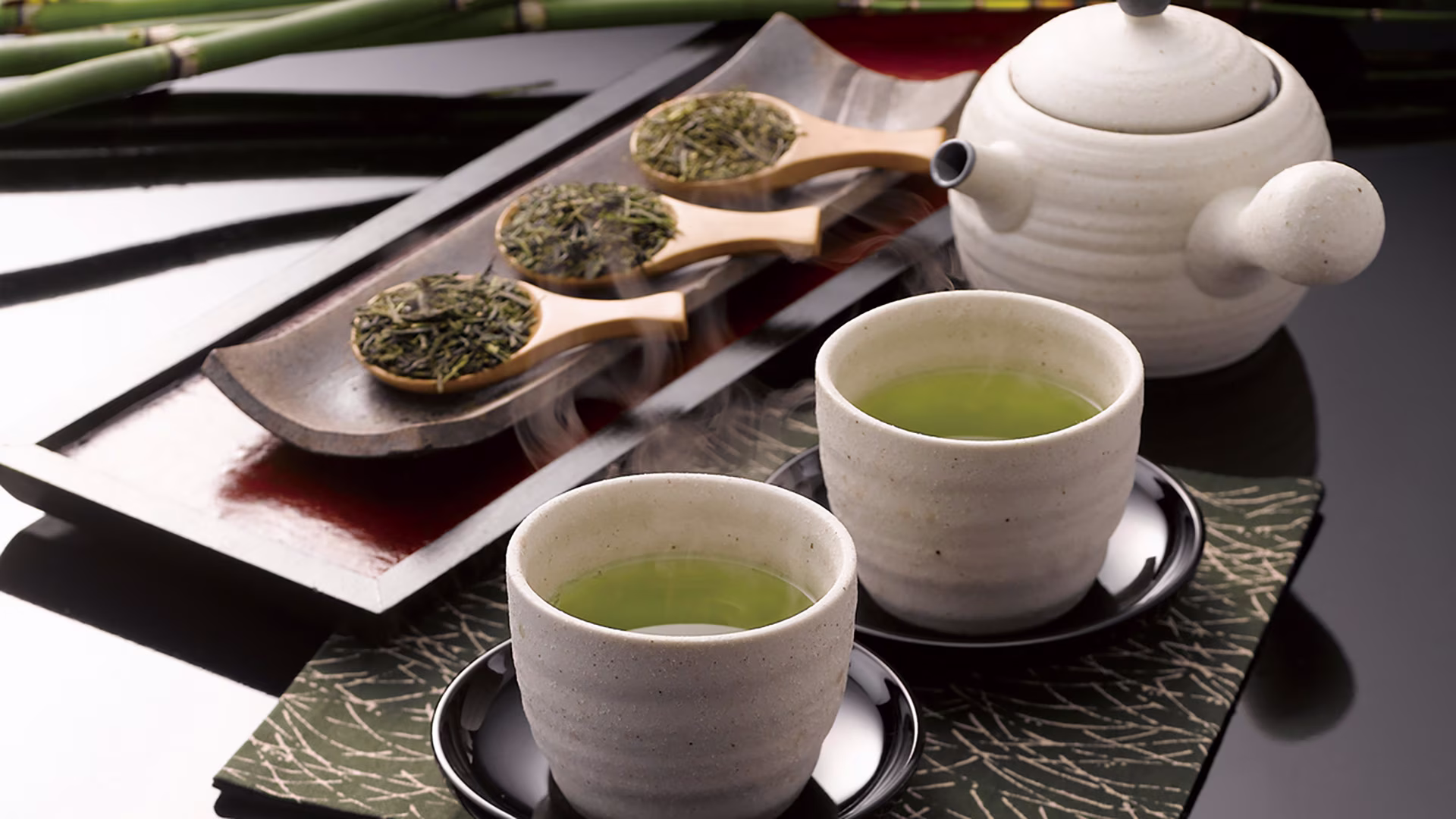 Japanischer Grüner Tee mit Teekanne, zwei Tassen, Bambus und losen Teeblättern auf Holzlöffeln