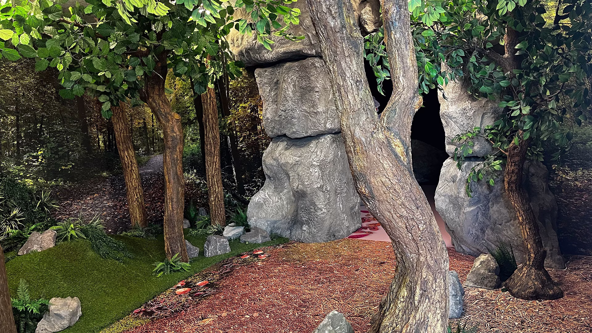 Naturnah gestalteter Felseneingang zwischen Bäumen und Pflanzen im Gerolsteiner Erlebnisbereich.