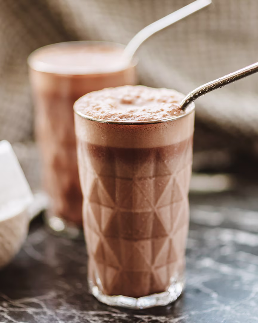 Cremiger Schoko-Soja-Shake im Glas, garniert mit Eiswürfeln und Kakao.