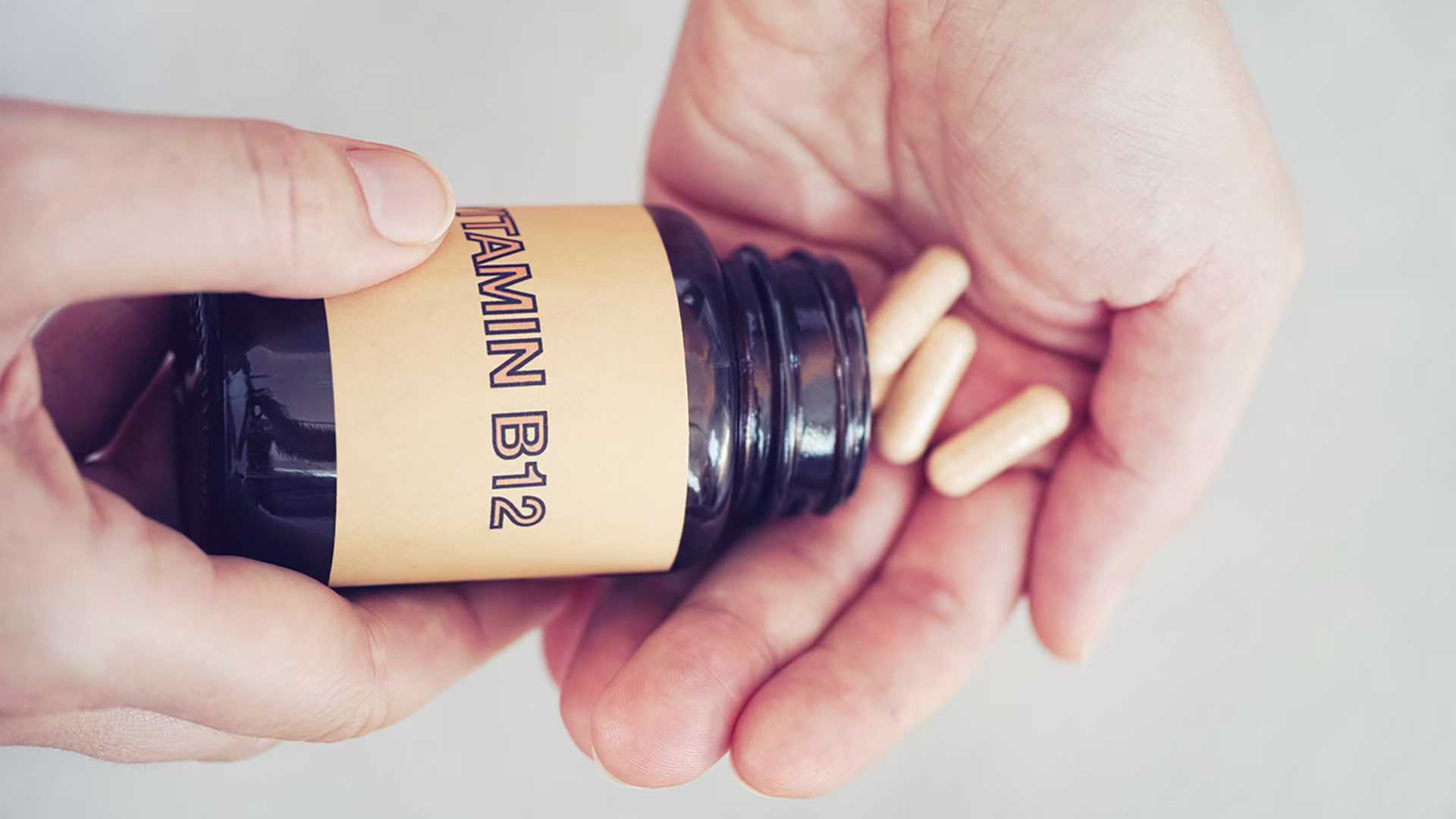 Nahaufnahme von Händen, die ein Vitamin-B12-Supplement aus Flasche nehmen