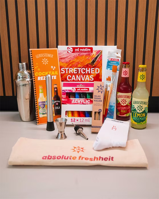 Gewinnspielset mit Cocktailzubehör, Farben und Pinseln, Leinwand, Gerolsteiner-Getränken (Watermelon Mint, Lemon Rosemary), Cocktail-Rezeptheft, Trinkhalmen, Socken und Handtuch mit „absolute Frische“-Schriftzug auf einem Tisch arrangiert.