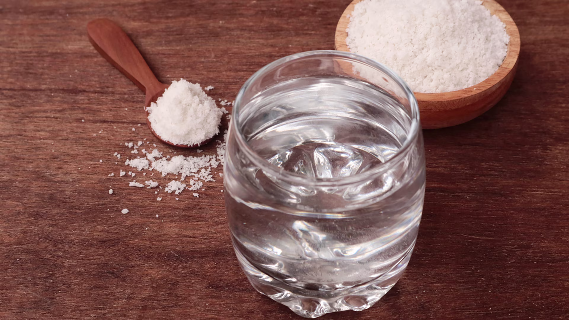 Glas mit Wasser sowie Löffel und Schale mit Elektrolytpulver.