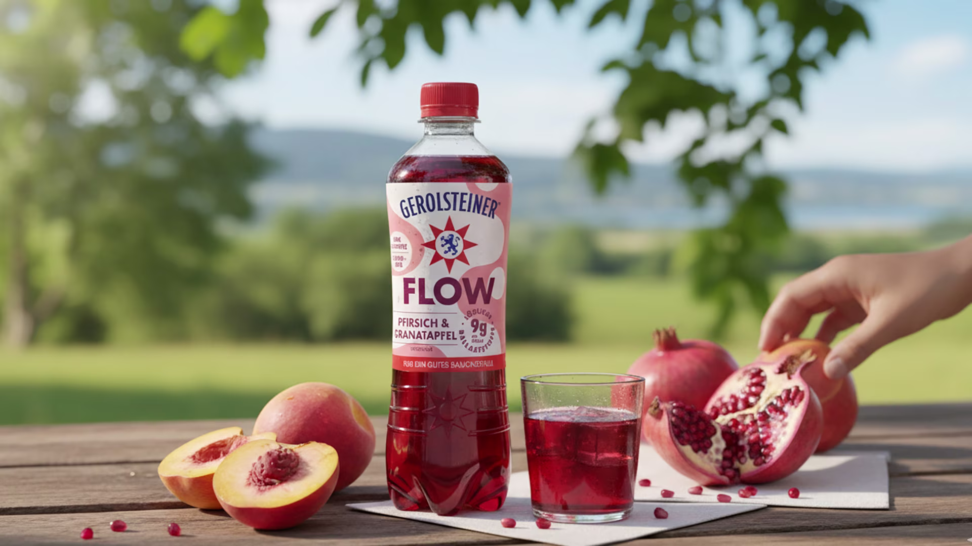 Eine Flasche Gerolsteiner Flow Pfirsich & Granatapfel steht auf einem Holztisch im Grünen. Daneben liegen halbierte Pfirsiche, Granatäpfel und ein Glas mit rotem Getränk. Eine Hand greift nach einem Granatapfel, im Hintergrund Natur und blauer Himmel.