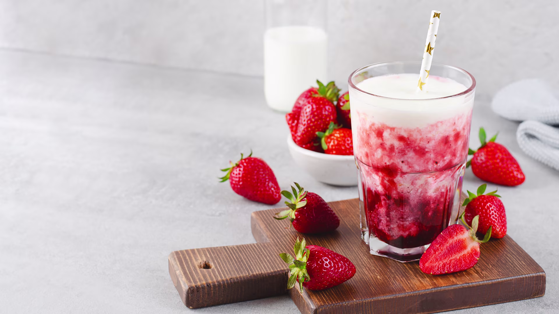 Glas mit Erdbeerpüree und Kefir auf einem Holzbrett. Drumherum liegen ganze Erdbeeren.