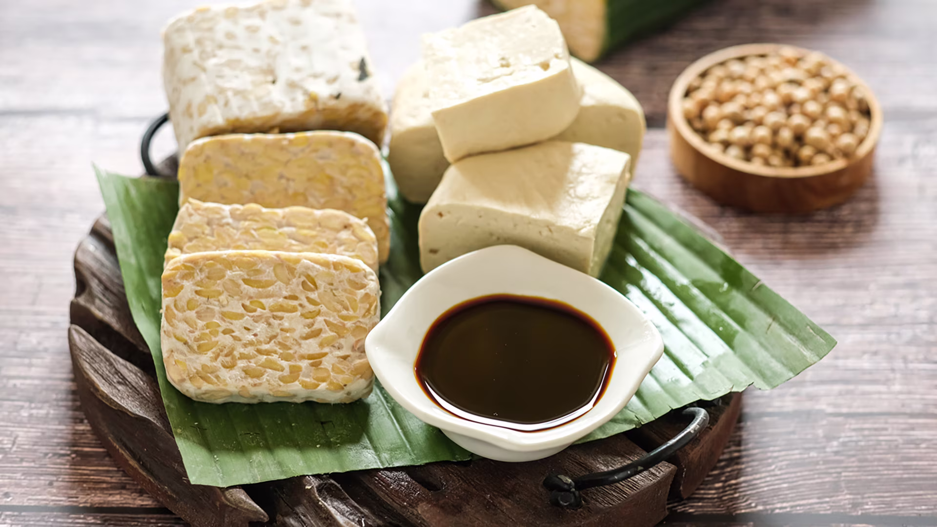 Tofu und Tempeh als vegane Proteinquellen mit Sojasoße angerichtet auf einem Holzbrett