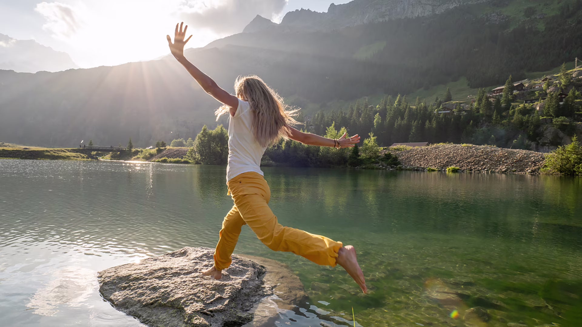 Eine Frau springt von Stein zu Stein über einen Bergsee