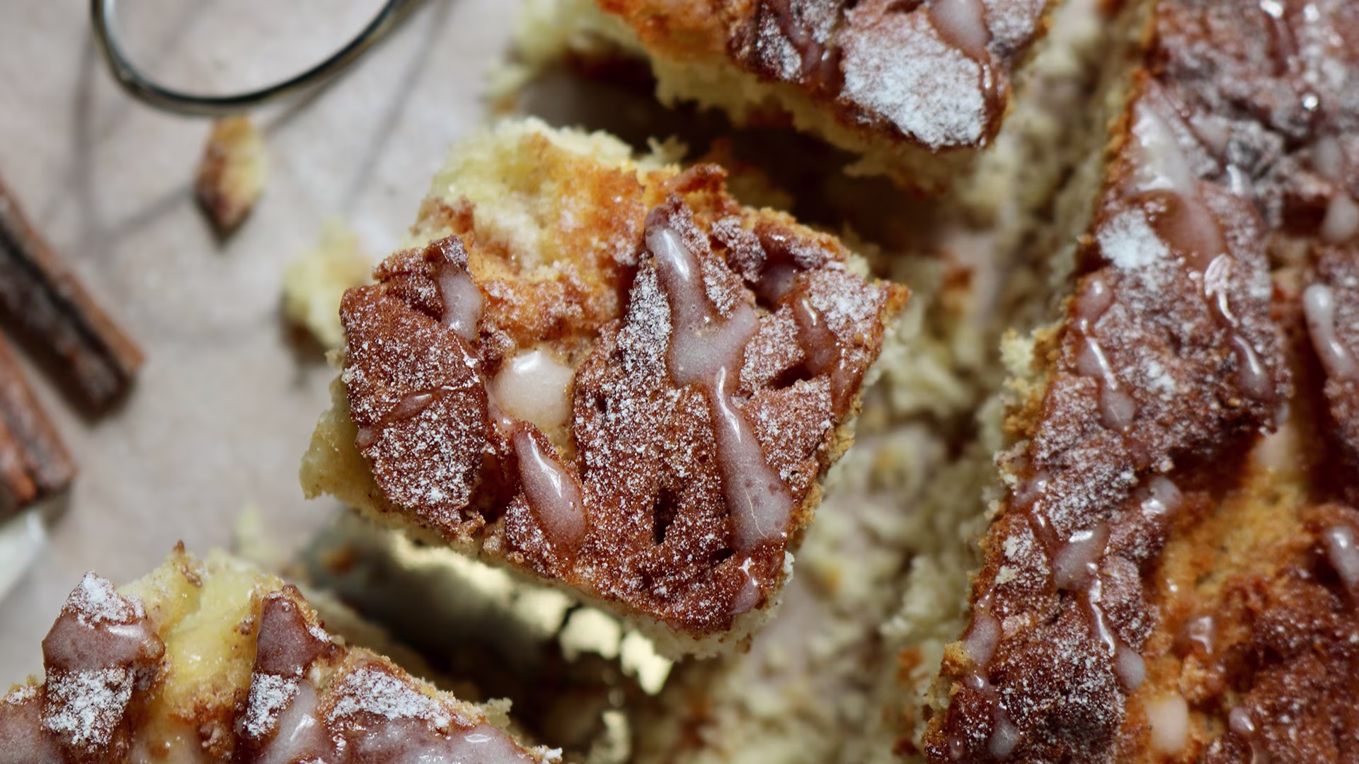 Nahaufnahme eines saftigen Zimtschneckenkuchens mit Zimt-Zucker-Kruste und Puderzuckerglasur, serviert in würfeligen Stücken.