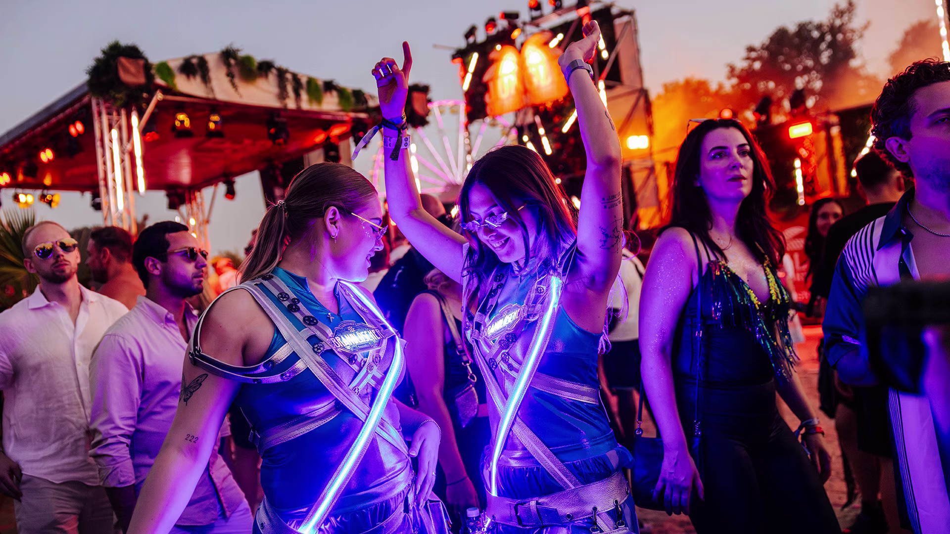Zwei Brandlöscher-Promoterinnen in leuchtenden Outfits tanzen ausgelassen vor einer Festivalbühne bei Nacht – umgeben von feiernden Menschen und stimmungsvollem Licht.