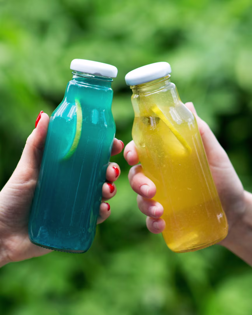 Zwei selbstgemachte Isotonische Getränke, einmal blau, einmal gelb, in kleinen Glasflaschen mit Schraubverschluss.