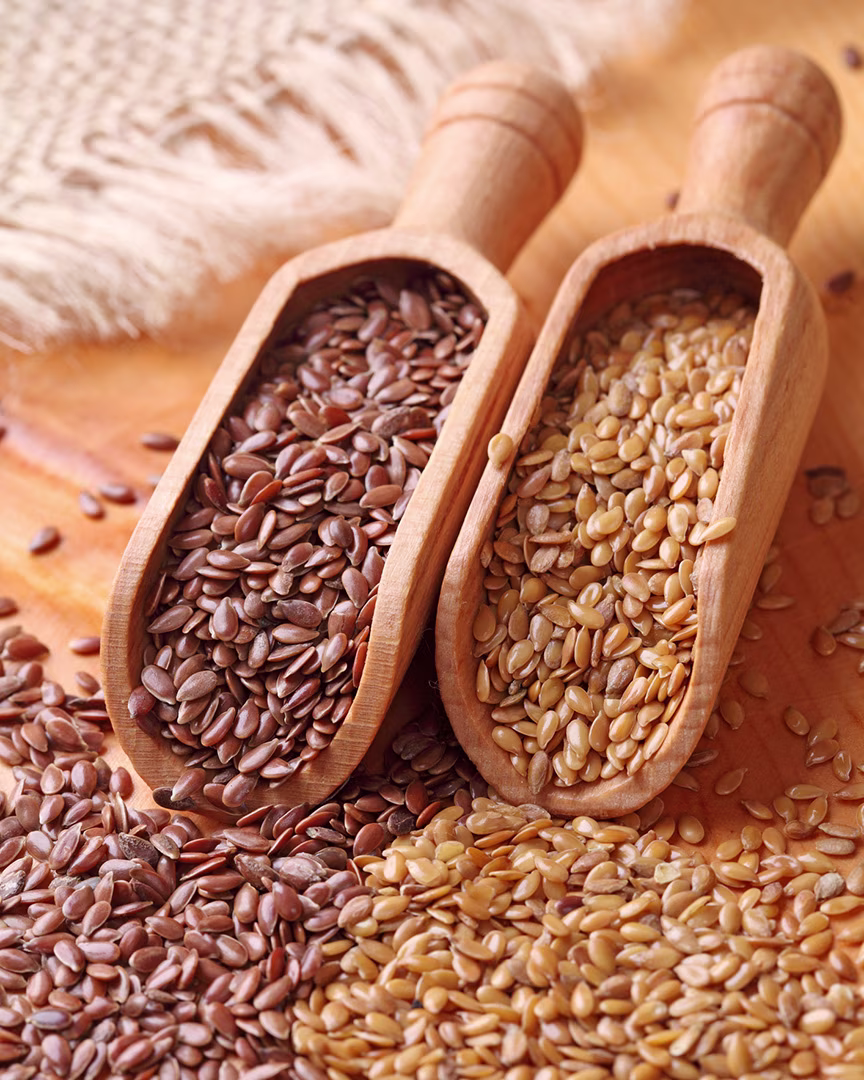 Goldene und braune Leinsamen in zwei kleinen Holzkellen auf hellem Holztisch