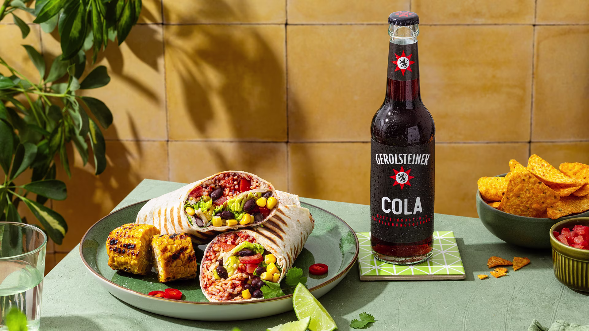 Herzhafte Burritos mit Reis, Bohnen, Mais und frischem Gemüse, serviert mit gegrilltem Maiskolben und knusprigen Nachos. Dazu eine gekühlte Gerolsteiner Cola für den perfekten Snack-Genuss.