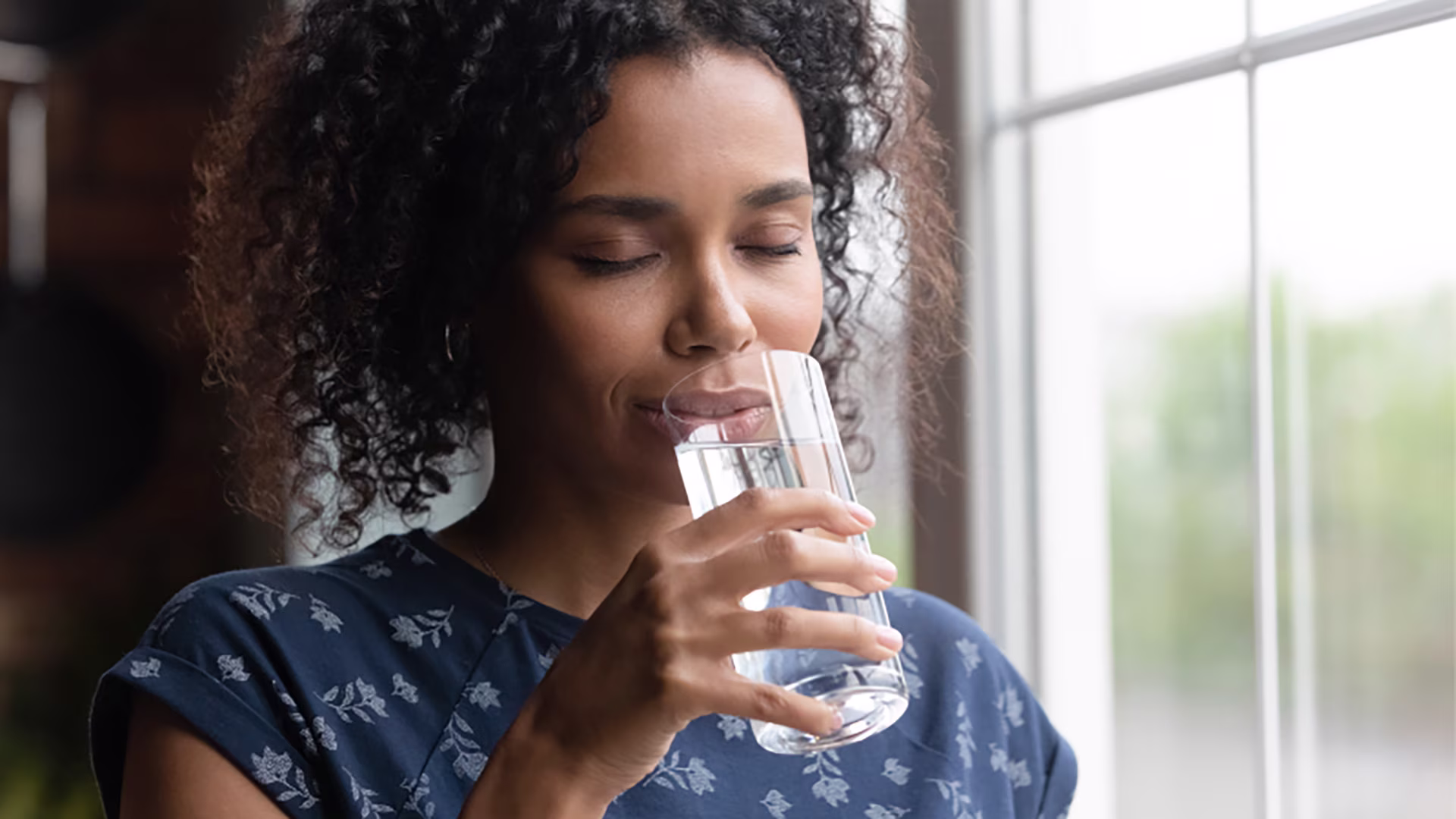 Une femme boit un verre d'eau en fermant les yeux.
