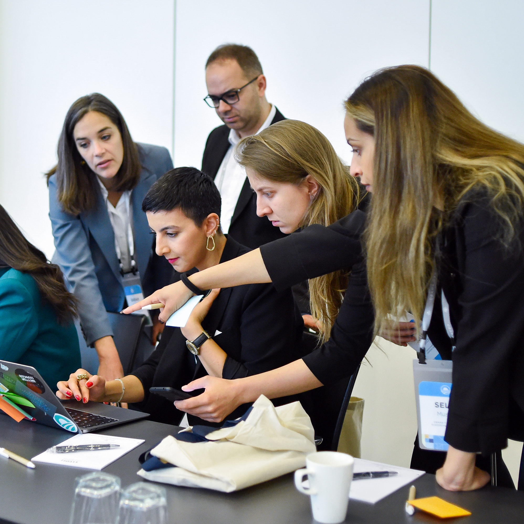 A group of people with a range of light to dark skin tones huddle around a table. They are all dressed professionally. On the table is a tent card with The Obama Foundation rising sun logo. 