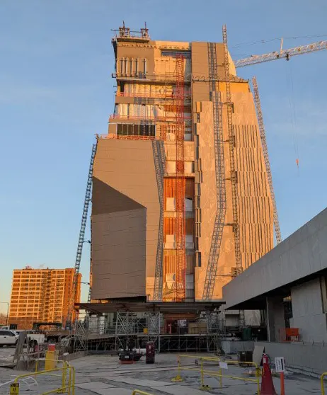 A multistory building under construction towers in golden sunlight. Cranes can be seen on each side as well as scaffolding.