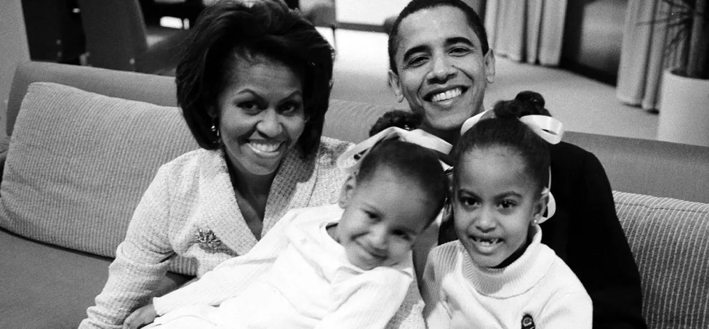 President and Ms.Obama sit with young sasha and malia in black and white.