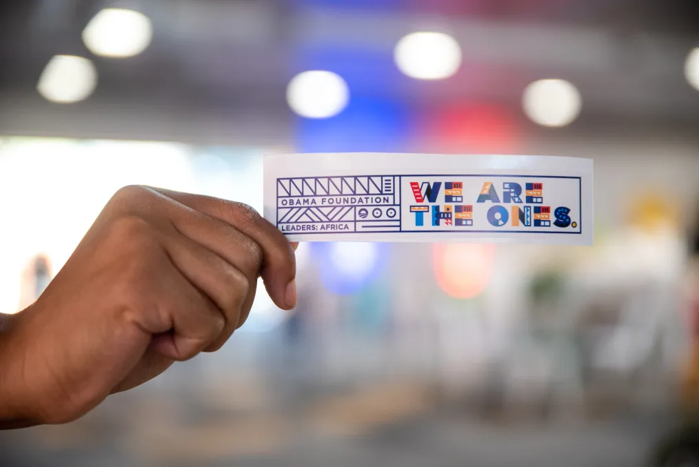 A hand holds a sticker that reads "We are the ones."