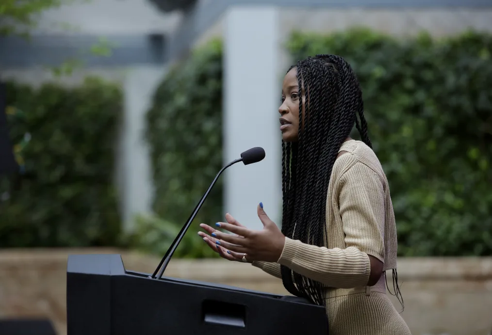 
Keke Palmer, a woman with a twist and deep skin tone stands over a podium giving a speech 
